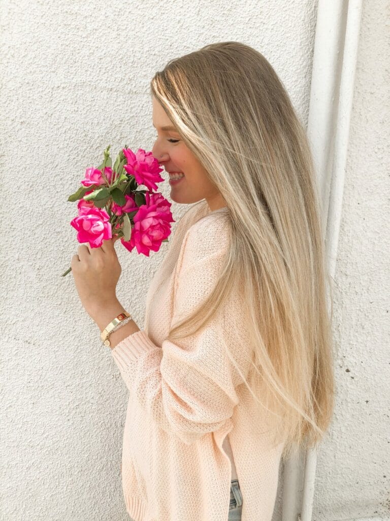 Peitho-Perfumes.ScentedCandles_ A woman wearing a pink sweater and pink flowers.